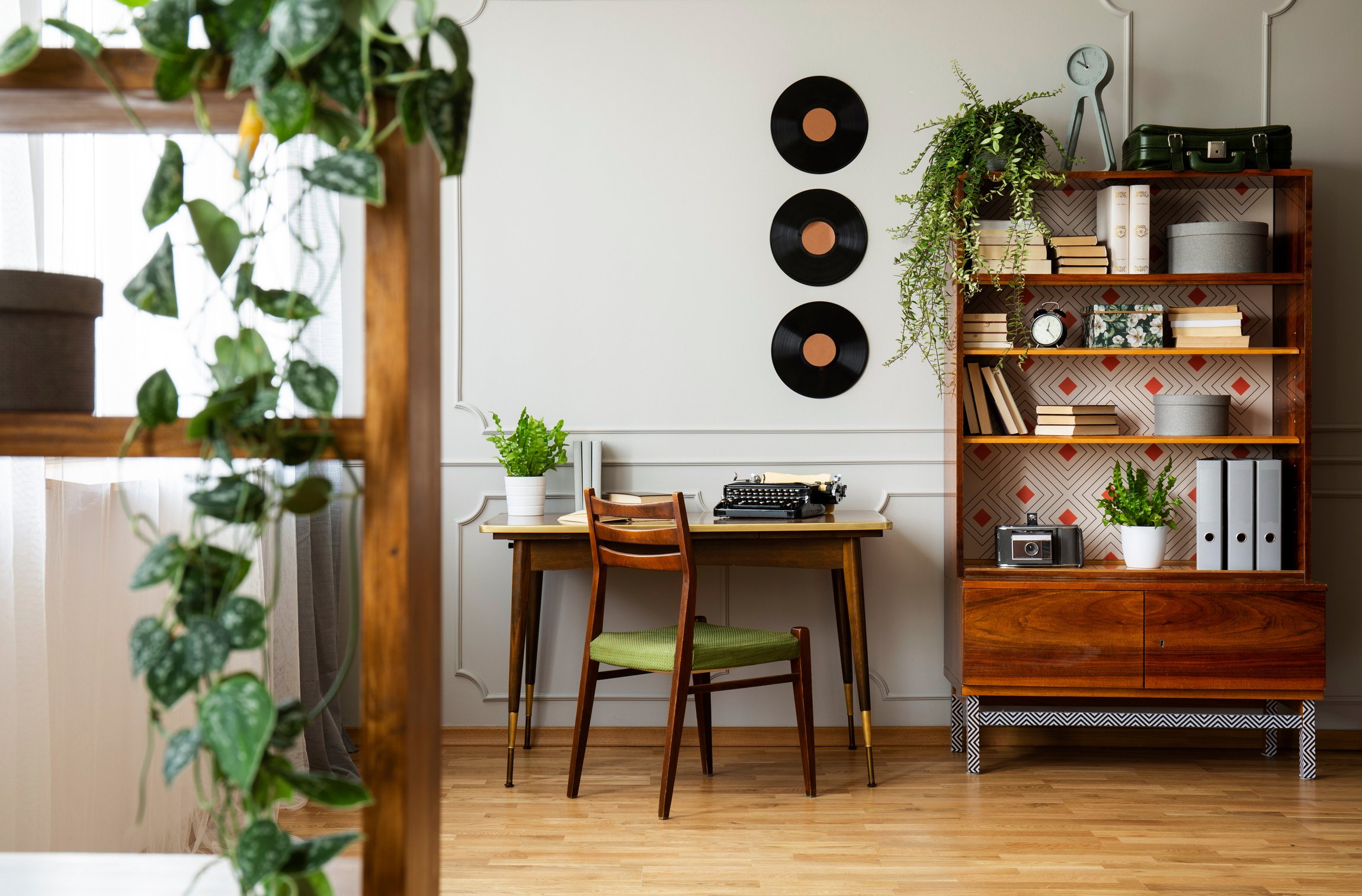 Black retro typewriter on a unique wooden desk, a mid-century modern chair and a renovated bookcase in a hipster home office interior. Real photo.